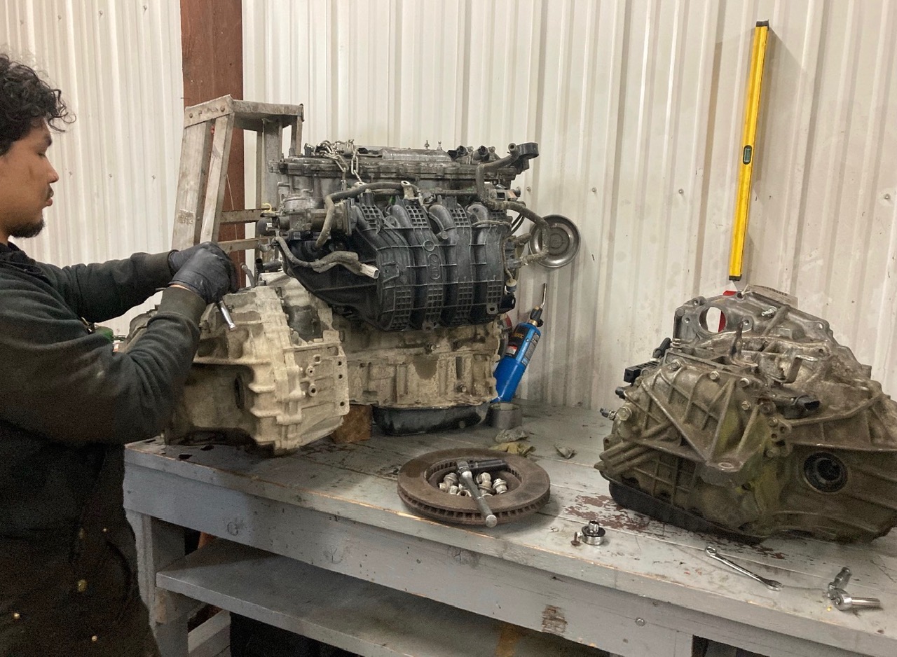 Technician working on an engine and transmission assembly at Plumb Easy